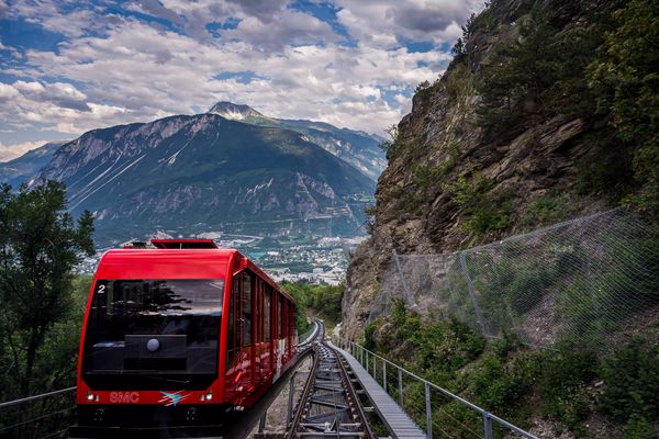 Red Swiss funicular from Sierre to Crans Montana, Valais Canton, Switzerland. Public transport cable car with scenic view over the city and mountain.