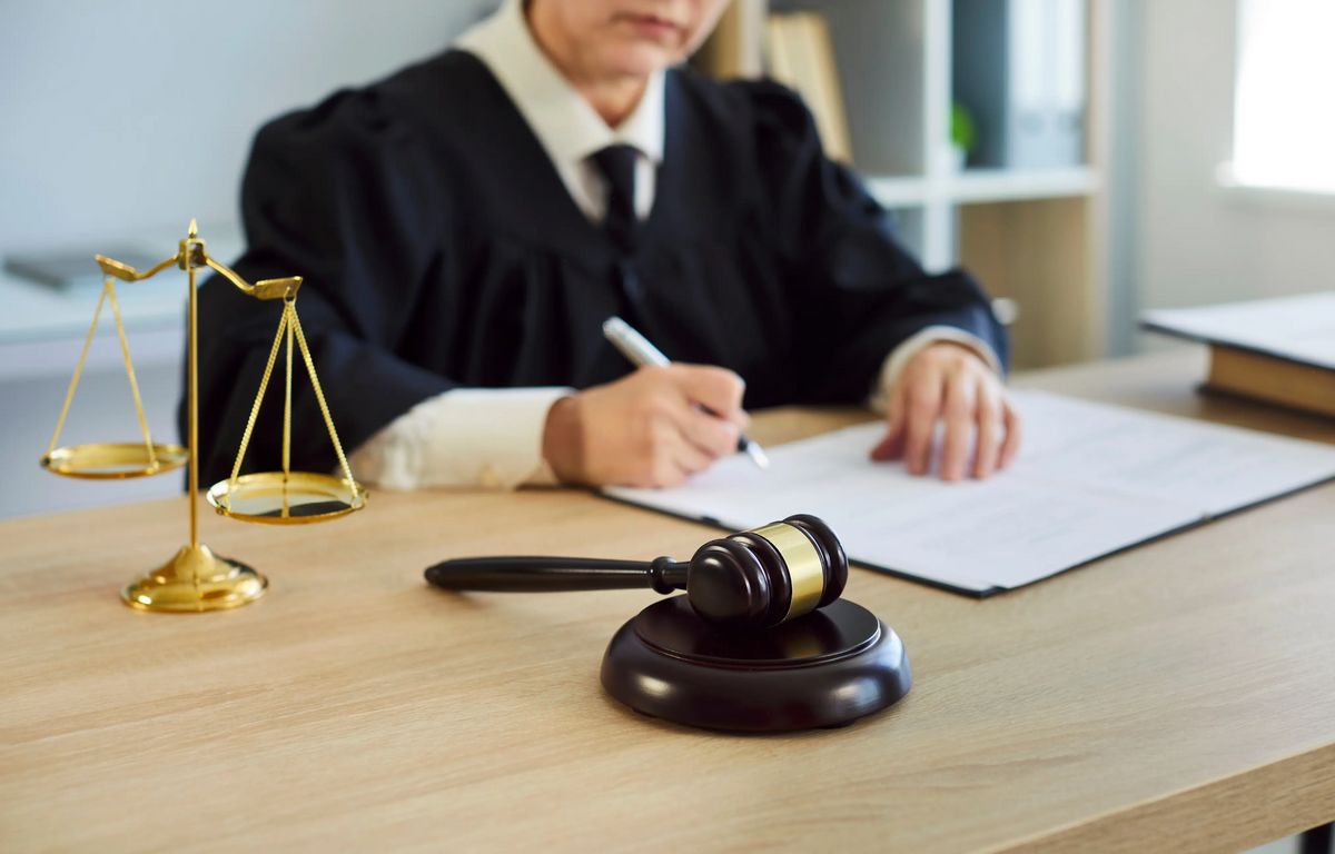 Female judge signing legal documents at courtroom desk with gavel and scales