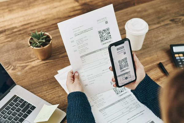 Woman paying invoice scanning QR code from document using fast secure payment system and smartphone QR scanner. Business woman paying bills using express payment technology. Paying expenses online
