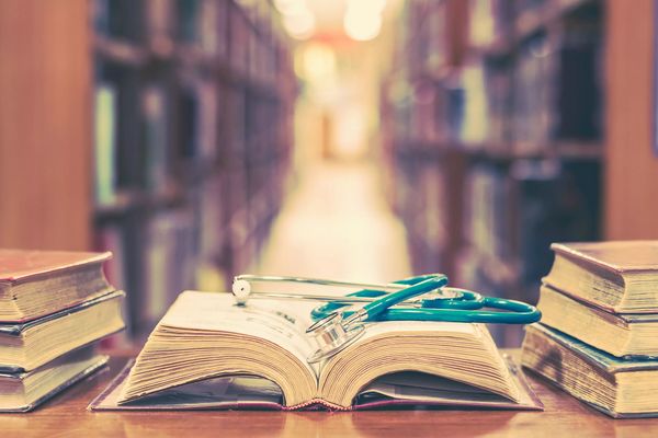 Old book in library with stethoscope on open textbook, stack pil